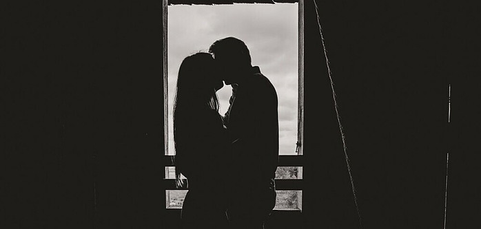 black and white image of a couple in an old barn kissing and holding one another