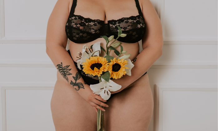 plus size woman in black lingerie holding a bouquet of sunflowers in front of her crotch/belly area