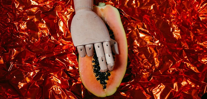 sexy suggestive image of a cut in half papaya with a wooden hand and 2 fingers bending inside of the papaya