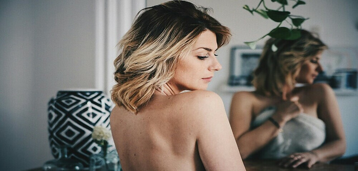 woman wrapped in blanket over her bust standing in front of mirror looking over her shoulder