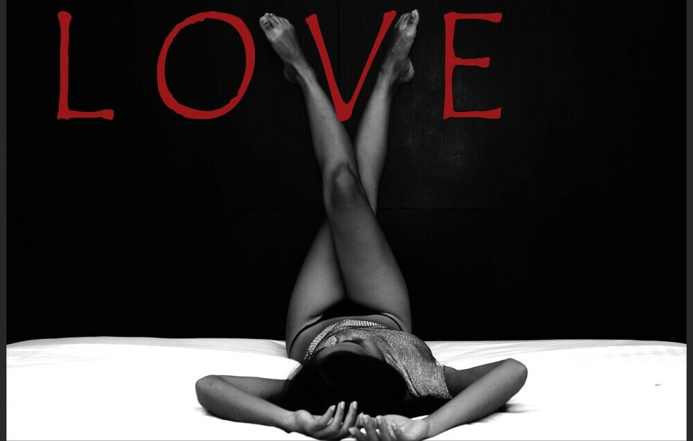 a black and white image of a woman laying on her back on a bed in lingerie with her legs crossed up the wall and the word LOVE written in red 