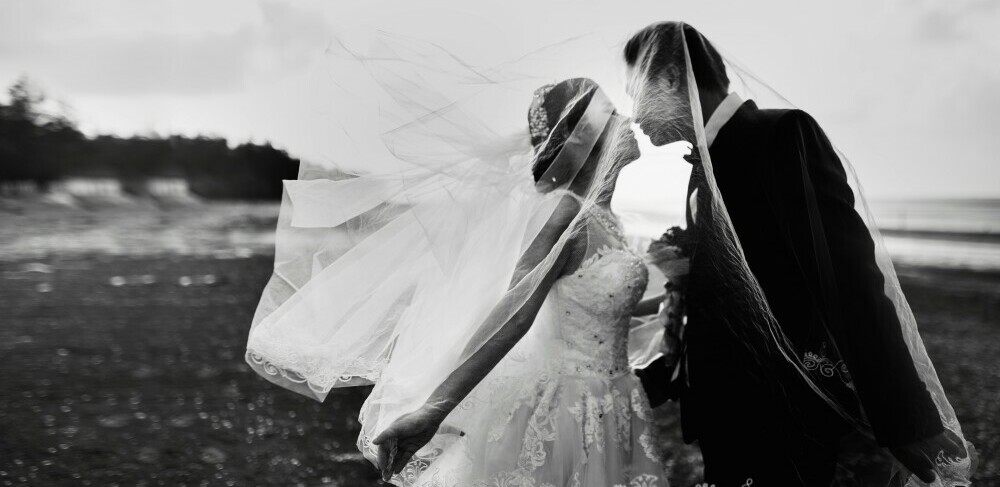 a bride and groom kissing underneath bride's veil in a black and white image