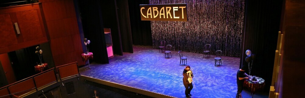 A lit theatre stage with a CABARET sign over it and a woman walking the stage