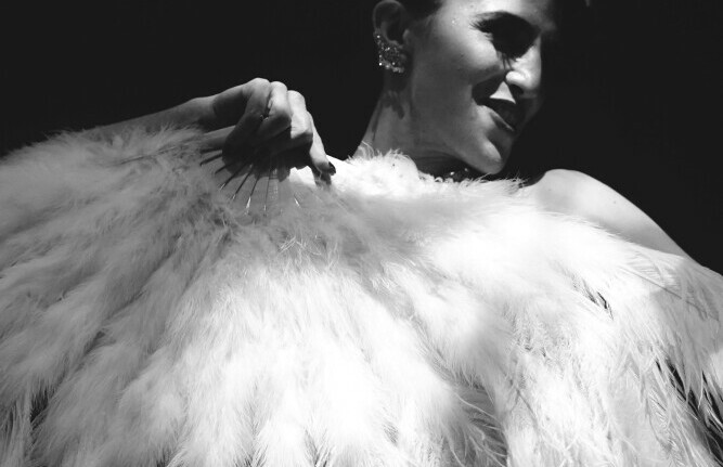 black and white image of a woman holding a huge feather fan in front of her body with a smile on her face-burlesque