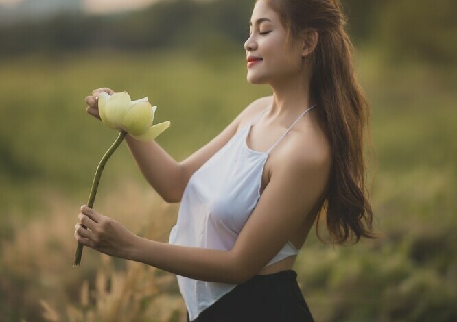 silk camisole worn by a woman with long hair standing in a field holding a large flower in her hands